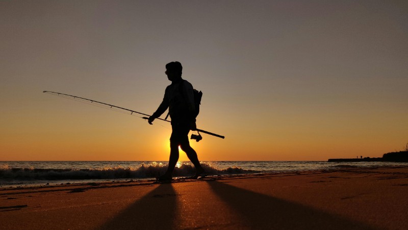 Silhouette of a man walking with a fishing rod along the beach during sunset., tags: für - pexel