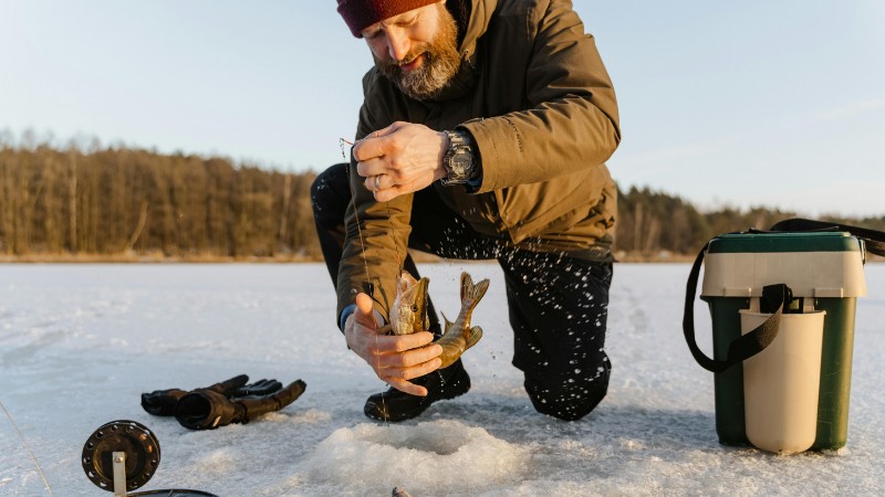 Man ice fishing on a frozen lake during winter, catching fish through a hole in the ice., tags: auf im flachen - pexel
